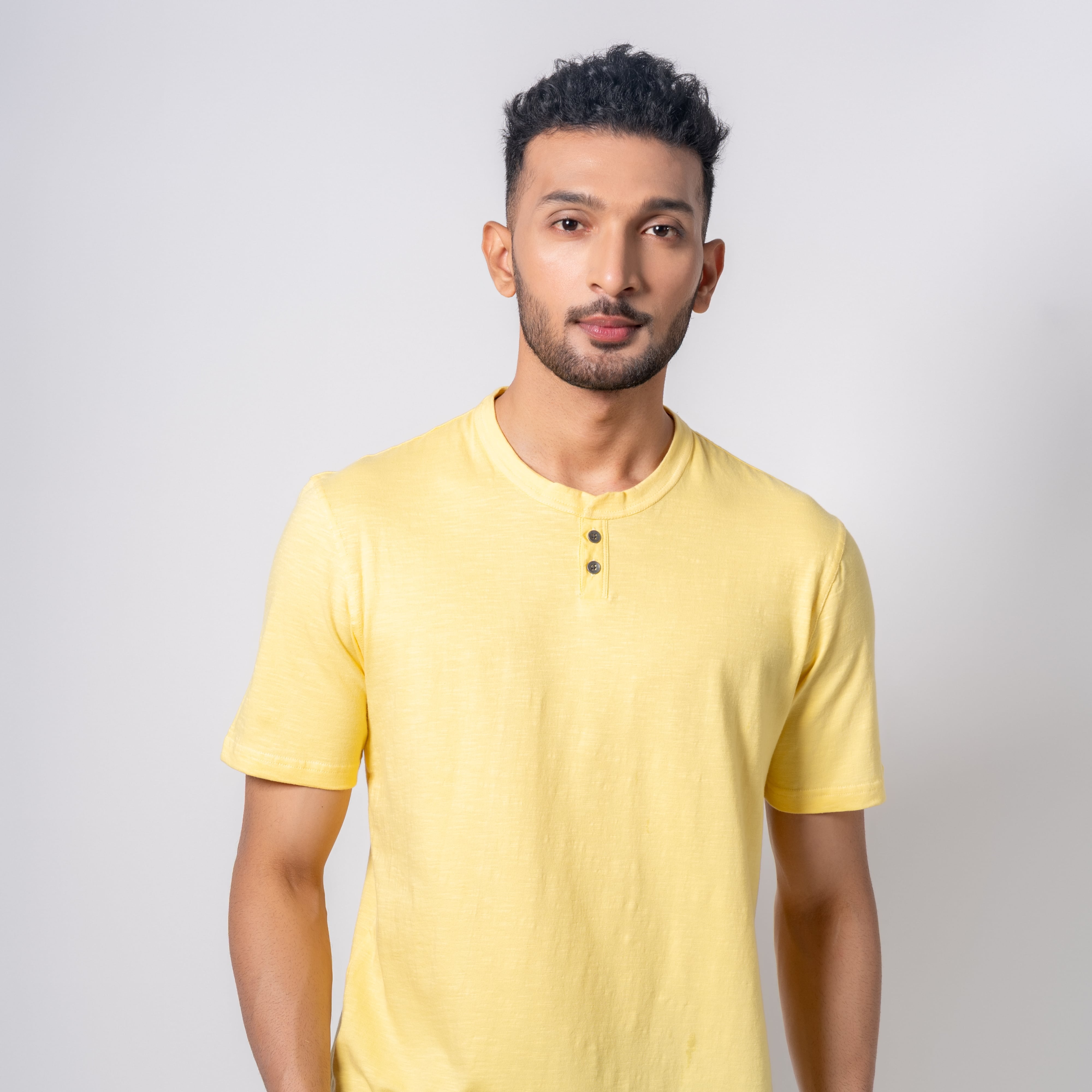 Man wearing a yellow henley shirt and black pants on a white background
