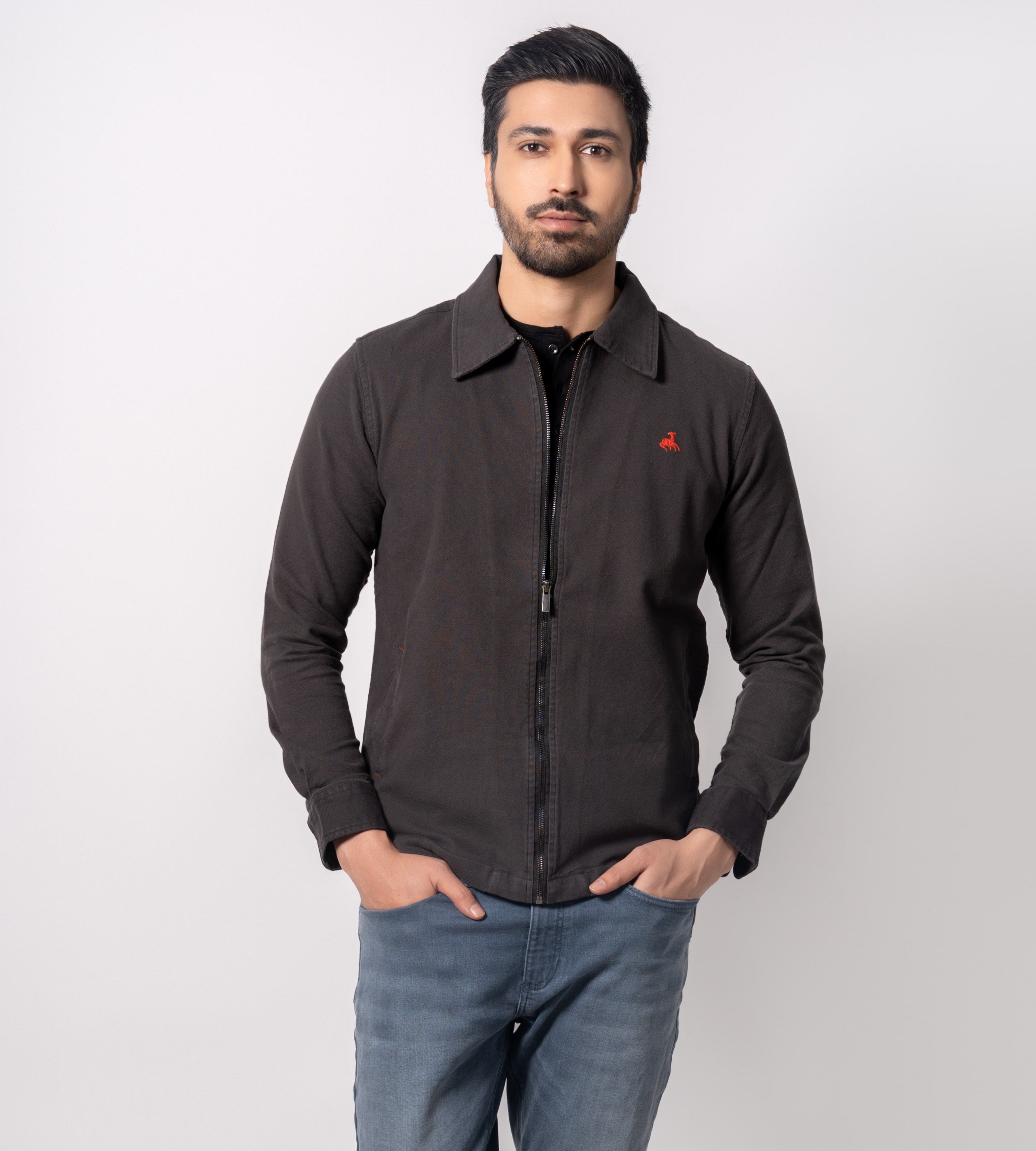 Man wearing a dark jacket with a red logo, blue jeans, and white sneakers on a white background