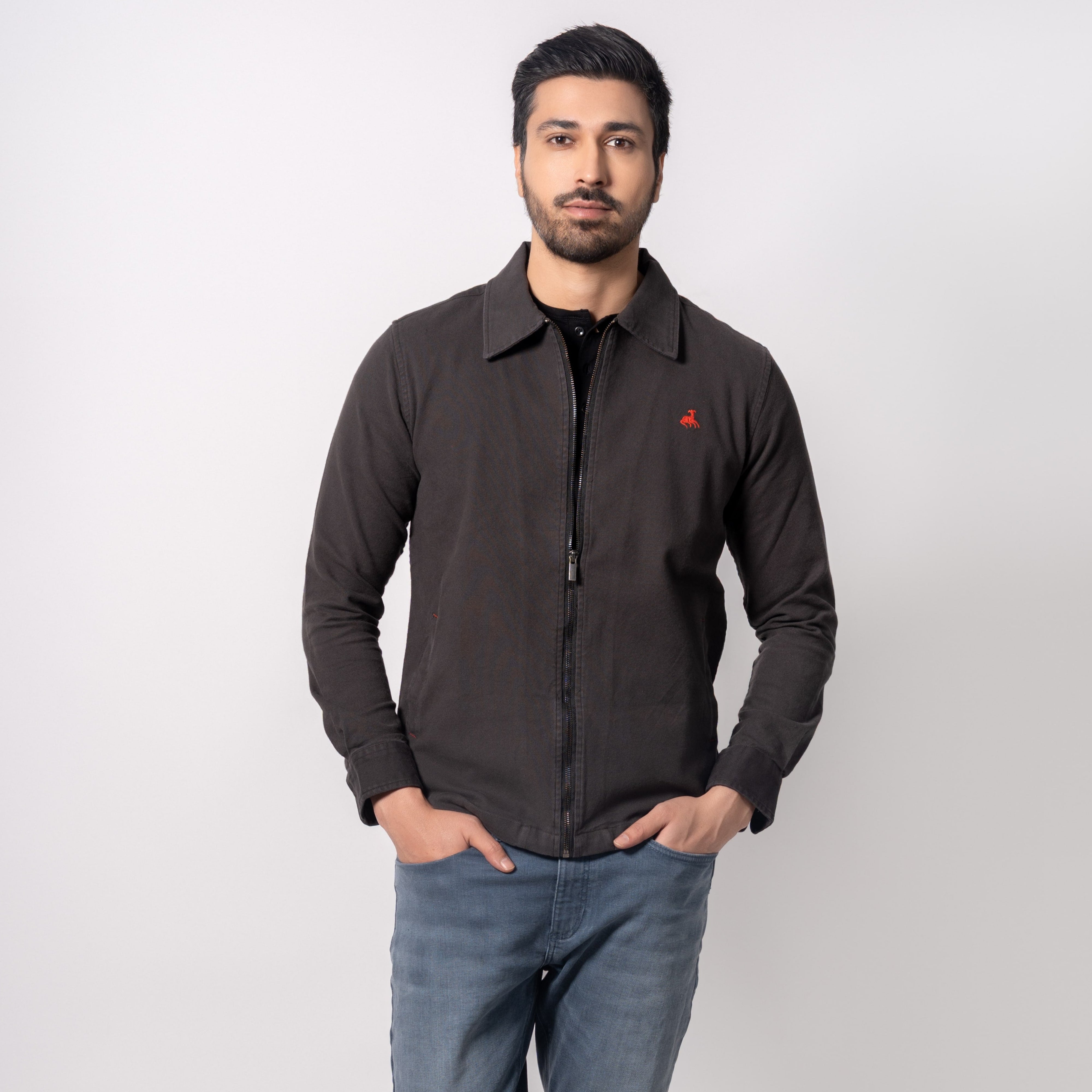 Man wearing a dark jacket with a red logo, blue jeans, and white sneakers on a white background