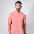 Man wearing a pink henley shirt and black pants on a white background