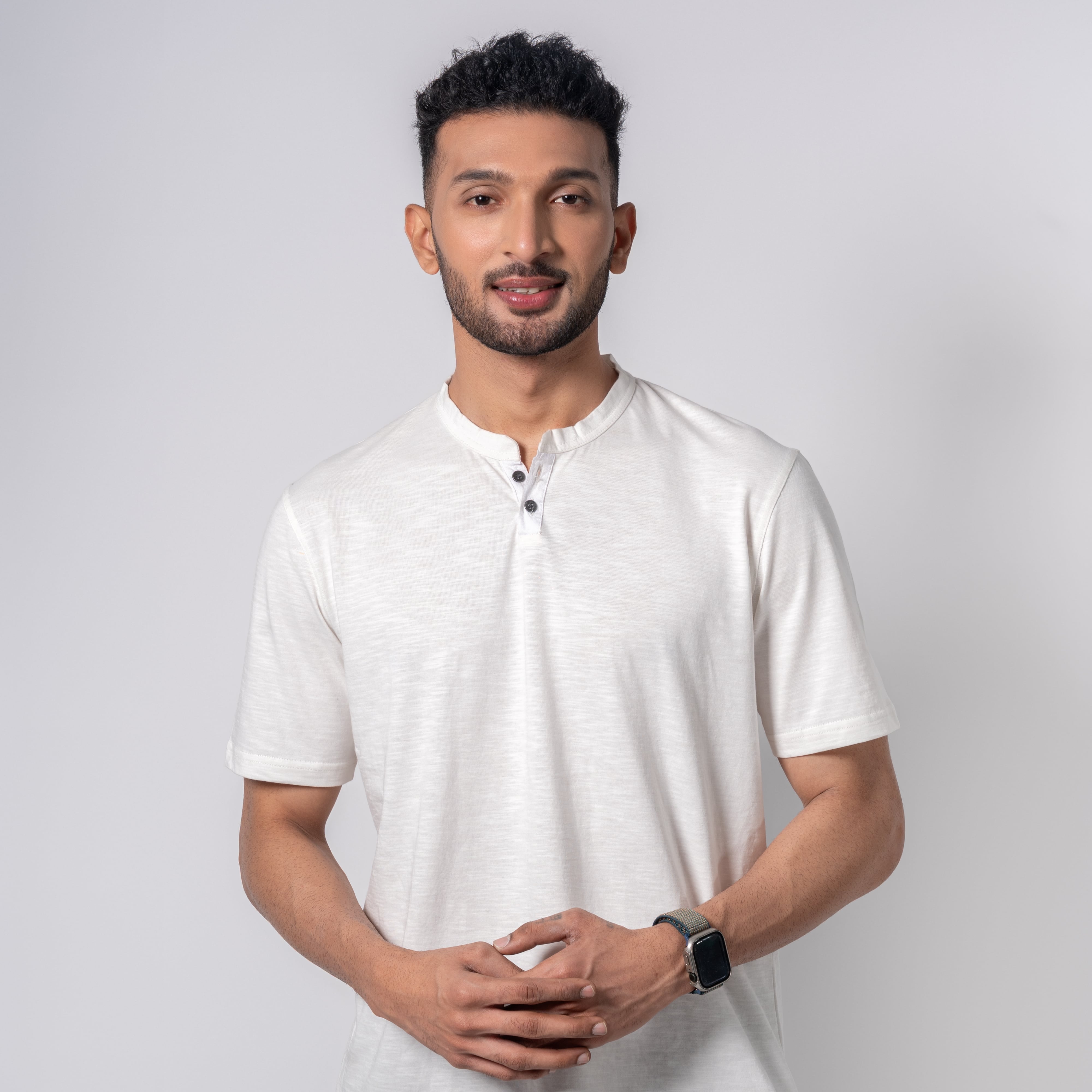 Man wearing a white shirt and dark pants against a plain background